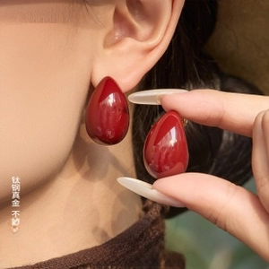 Detail of drop-shaped dark red enamel earrings with gold-plated titanium steel finish