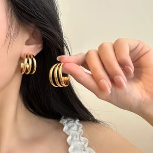 Detail of three-layered gold titanium steel hoop earrings worn on female ear model
