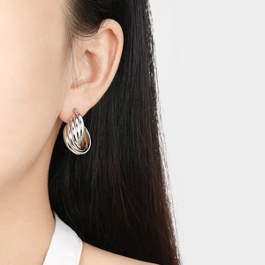 Close-up of interlocking silver titanium steel hoop earrings on a female model