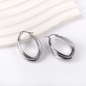 Detailed view of silver triple-layered oval hoop earrings on a white wavy pedestal