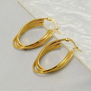Macro detail of triple-layer gold oval hoop earrings with beaded clasp on gray fabric