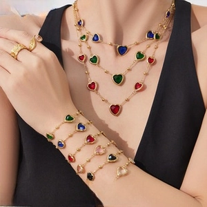 Detail of layered gold necklaces and bracelets with colorful heart-shaped crystal pendants