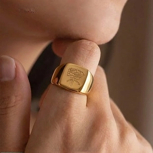 Macro shot of gold square signet ring featuring intricate floral engraving on polished metal