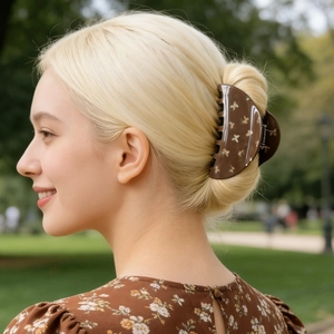 Detail of large brown hair claw clip with white butterfly print on a messy hair bun