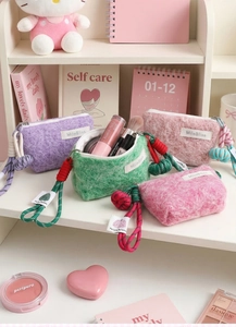 Detail of colorful fluffy coin pouches with woven lanyards and brand label on shelf