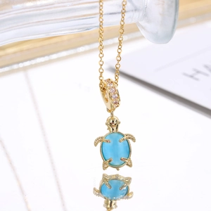 Macro shot of gold turtle pendant with sky blue opal stone and zircon bead on a chain