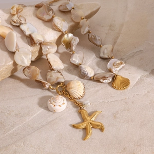 Detailed close-up of shell necklace with gold starfish and pearl on beach sand background