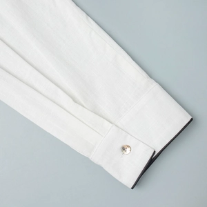 Détail de la manchette en lin blanc avec passepoil foncé et bouton en nacre naturel