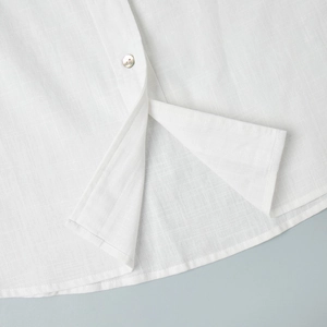 Détail de chemise en lin blanc avec fente latérale, bouton nacré et texture de tissu