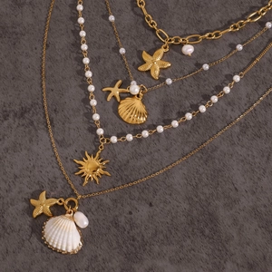 Macro shot of layered gold shell necklaces with starfish and pearl charms on stone