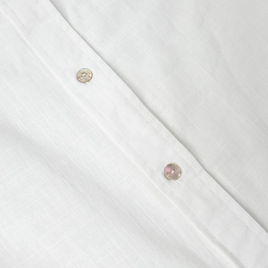 Détail d'une chemise en lin blanc montrant la texture naturelle et les boutons nacrés