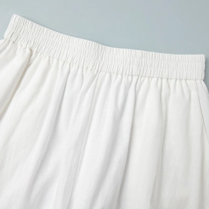 Détail d'un short en lin blanc avec taille élastique et plis fins, texture naturelle