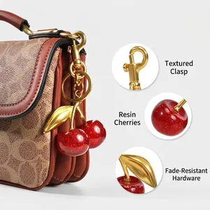 Sparkling red resin cherry keychain accessory with gold leaves on a luxury brown handbag