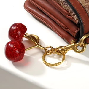 Glittery red resin cherry keychain with golden metal leaf detail on luxury leather bag