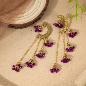 Detail of vintage gold alloy earrings with purple beads and ethnic bell tassel pendants