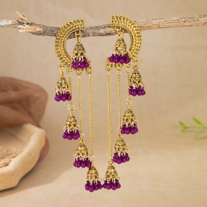 Detailed shot of golden hollow Jhumka earrings with purple beads on a branch