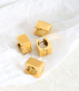 Detailed view of square gold hoop earrings on white textured paper background