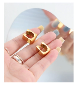 Detail shot of shiny golden square hoop earrings held against a mirror background