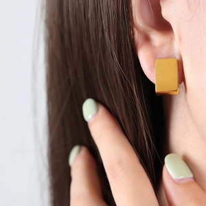 Minimalist golden square hoop earrings with a polished finish worn on a model's ear