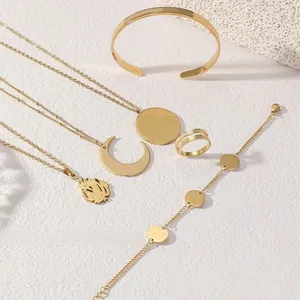 Flat lay of gold plated jewelry set including moon necklace, bracelet and ring on white stone