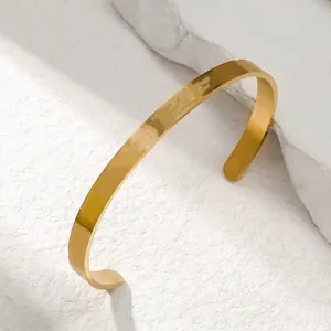Close-up of a minimalist golden stainless steel open cuff bracelet on white stone