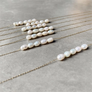 Detail of delicate gold chains with irregular baroque pearls on a stone background
