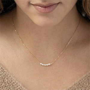 Gold stainless steel necklace with five freshwater pearls worn on a cozy sweater