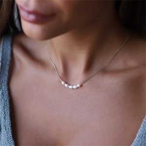 Close-up of minimalist gold-plated necklace featuring five curved white freshwater pearls