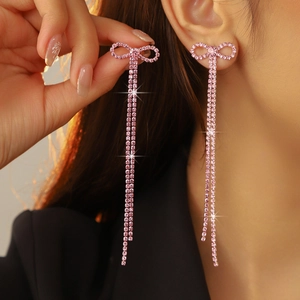 Detailed view of pink rhinestone bow earrings with long shimmering tassel chains