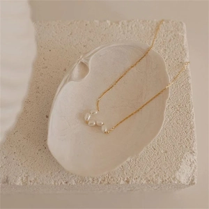 Detail of five freshwater pearls on a gold chain inside a white shell and stone