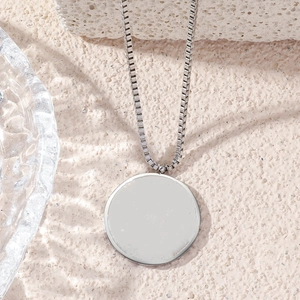 Close-up of minimalist silver round pendant with box chain on textured stone surface