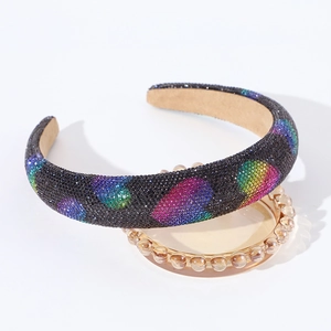 Close-up of a wide padded headband with sparkling rainbow rhinestones on a glass tray