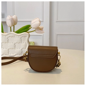 Close-up of brown leather mini saddle bag with gold metal buckles on a table