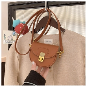Detail of a brown mini saddle bag featuring a matte gold twist lock and leather strap