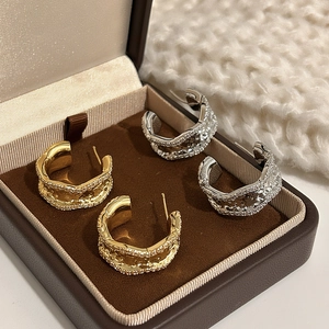 Irregular textured metal hoop earrings in gold and silver finish on a jewelry box