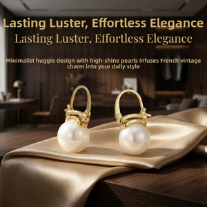 Detail shot of pearl huggie earrings resting on gold silk fabric in elegant soft light
