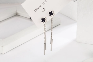 Detailed close-up of silver long tassel earrings with black clover studs on a display card