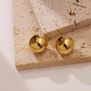 Polished gold hollow dome earrings shown on a beige travertine stone background