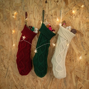 Three knit Christmas stockings in red, green, and cream hanging on a wooden background