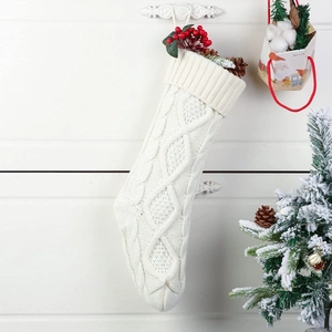 Macro detail of white cable-knit Christmas stocking with pine cones and red berries