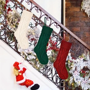 Three large knit Christmas stockings in ivory, green, and red hanging on a decorated staircase
