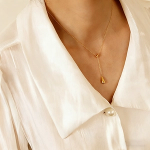 Close-up of gold plated teardrop pendant necklace on model wearing a white silk blouse