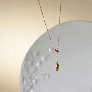 Elegant gold plated Y-shaped water drop pendant necklace on a decorative ceramic plate