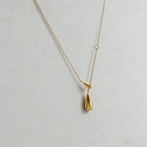 Macro shot of polished gold-plated teardrop pendant on a delicate cable chain necklace