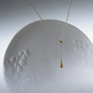 Macro shot of minimalist gold drop pendant and fine chain on floral ceramic plate