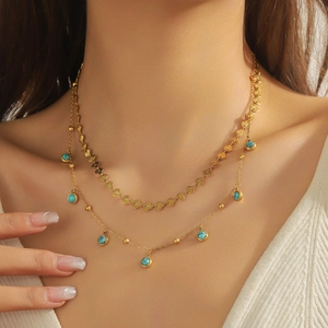 Close-up of double-layered gold necklace featuring heart elements and turquoise beads