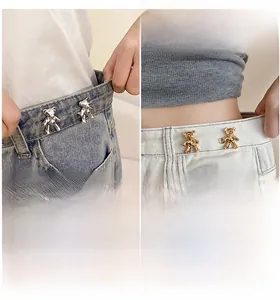 Detail showing bear-shaped metal waist adjusters in gold and silver on denim jeans