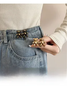 Detail of bear-shaped metal waist adjusters in bronze and gold on light blue jeans