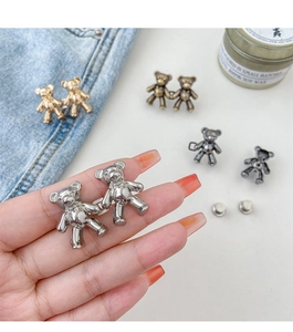 Detail of bear-shaped metal waist adjusters for jeans in silver, gold, and bronze tones