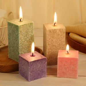 Set of four textured pillar candles in green, brown, purple, and pink on a wood table